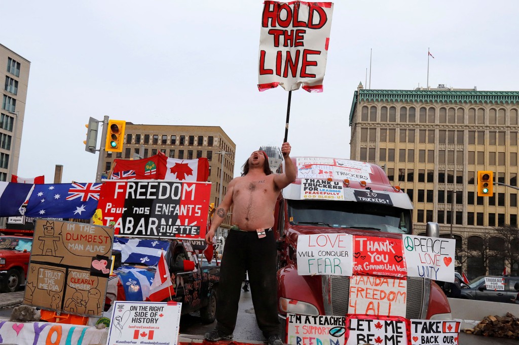 شخص يحمل لافتة أمام الشاحنات التي تغلق شارعًا في وسط المدينة بينما يواصل سائقو الشاحنات وأنصارهم الاحتجاج ضد تفويضات لقاح فيروس كورونا (COVID-19) في أوتاوا ، أونتاريو ، كندا.